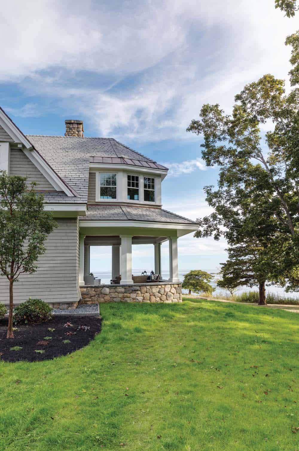 Covered porch with a fieldstone wall and white columns overlooking the ocean