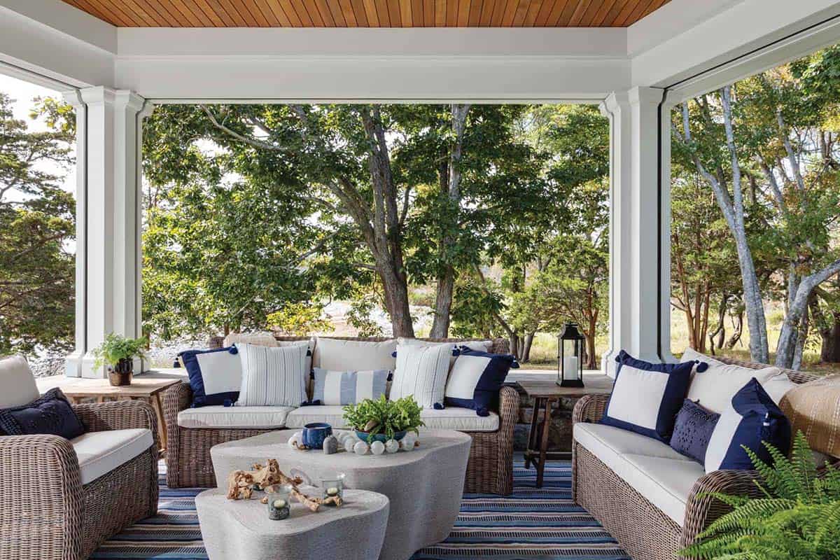 Porch seating area with wicker sofas, navy and white pillows, and a striped rug beneath a wood ceiling