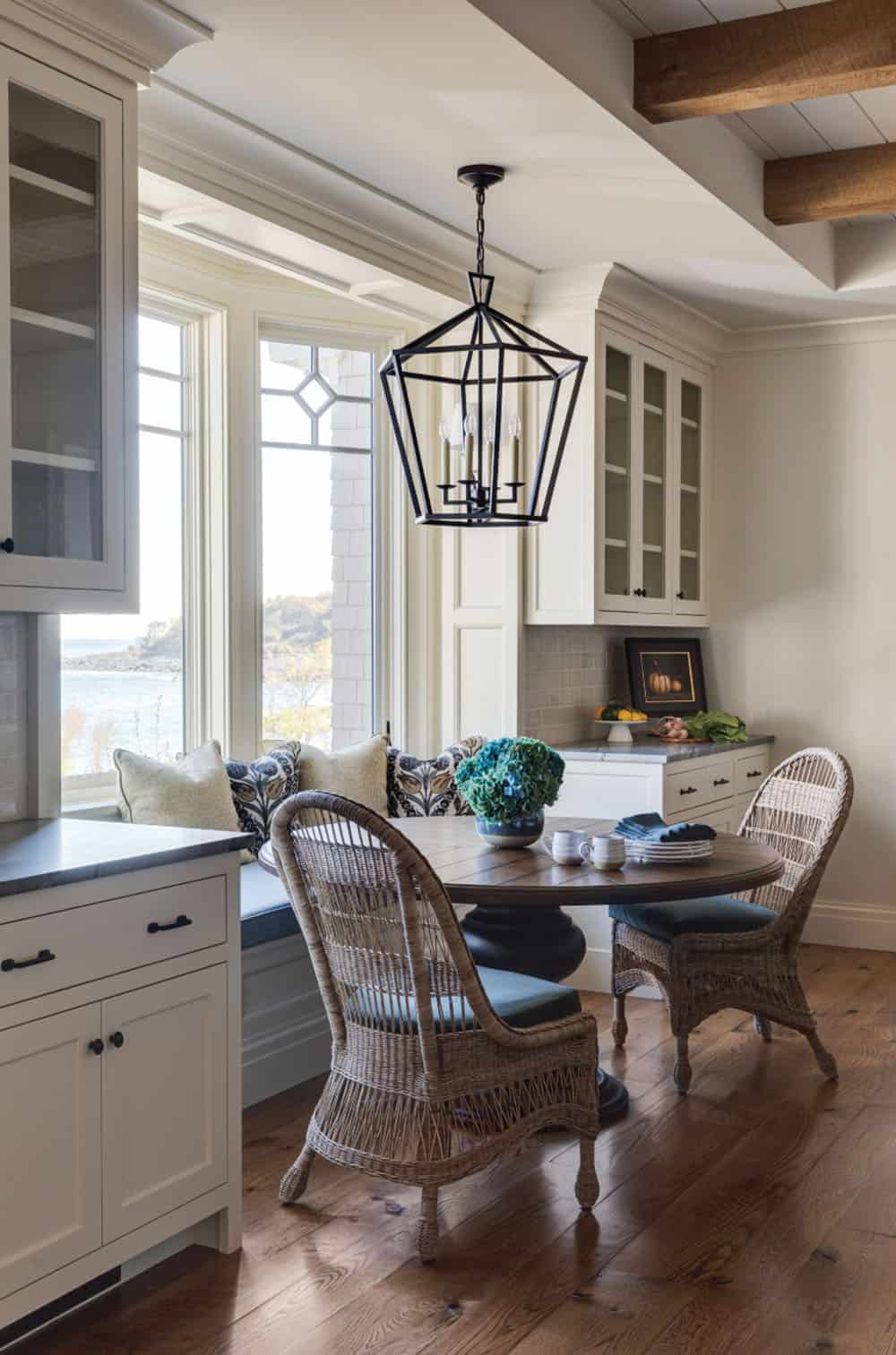 Breakfast nook with a built-in bench, round table, wicker chairs, and an ocean view through leaded-glass windows