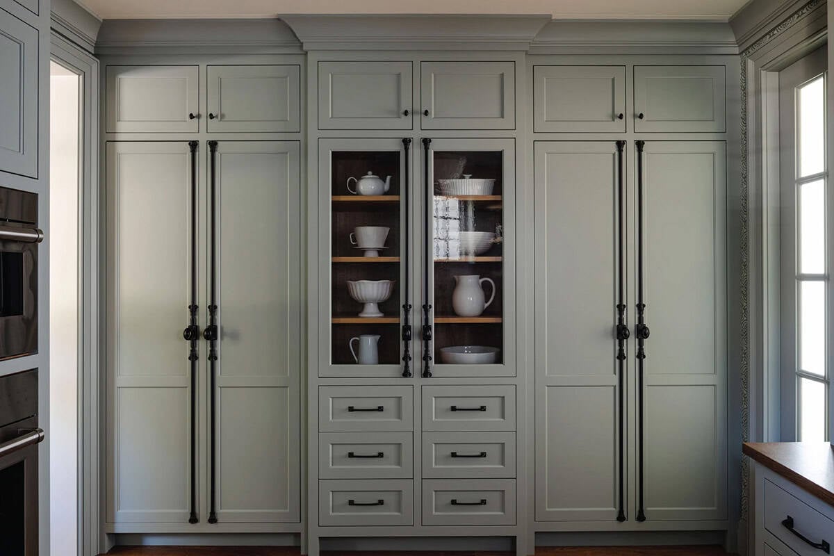 Sage green built-in pantry cabinetry with glass-front center doors and long black iron pulls