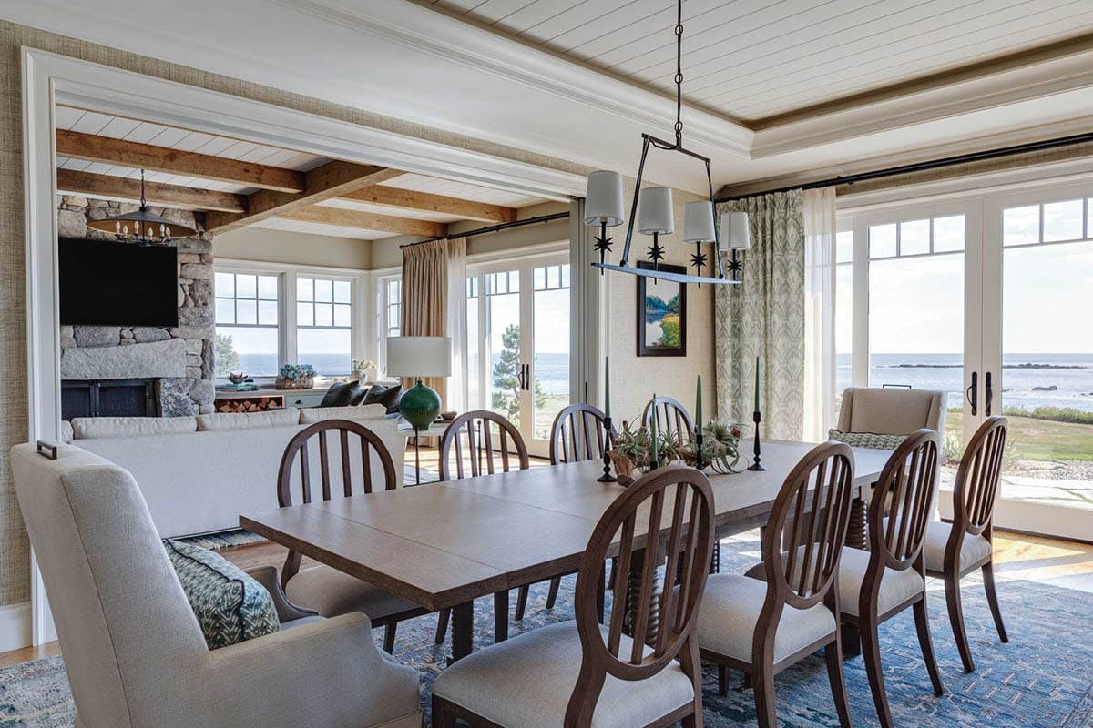 Dining area with a wood table and slat-back chairs, with French doors opening toward the sea