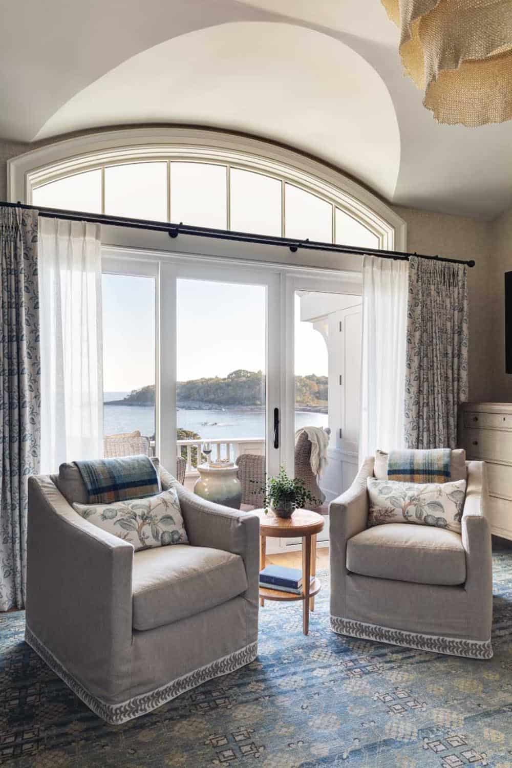 Bedroom sitting area with two slipcovered armchairs, a barrel-vaulted ceiling, and an arched window over sliding doors to the water
