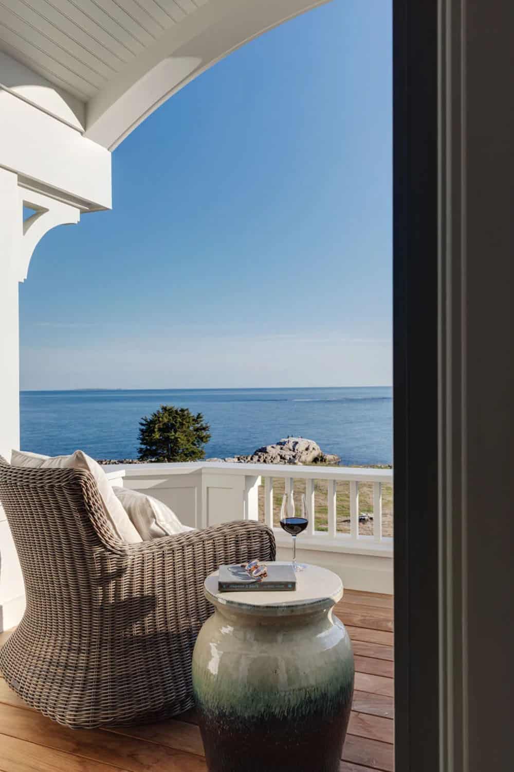 Private balcony with a wicker chair, ceramic side table, and a glass of red wine facing the ocean