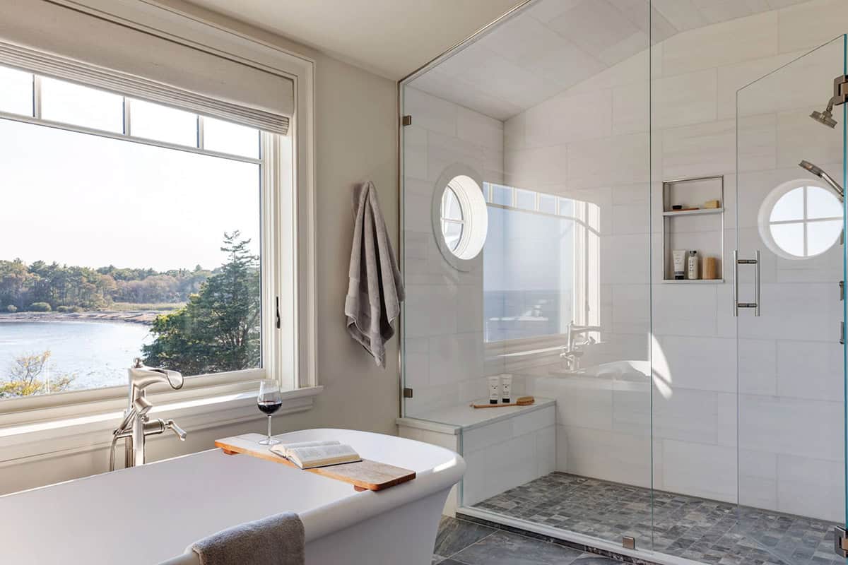 Bathroom with a freestanding tub by a window, a glass-enclosed shower with round windows, and gray stone floor tile