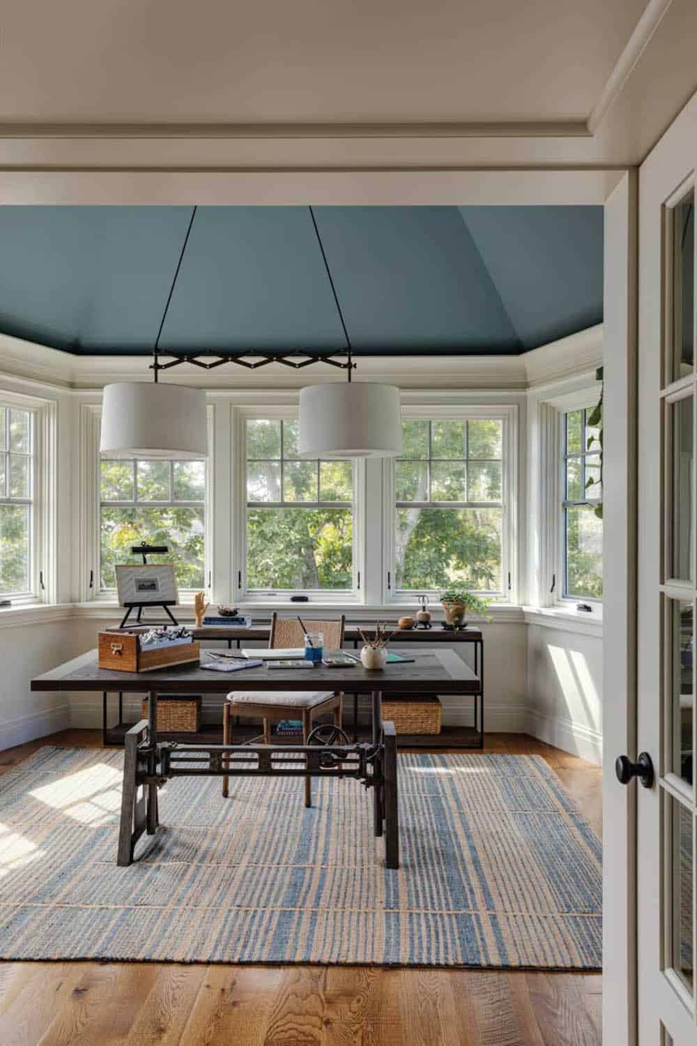 Home office with a blue-painted ceiling, an industrial-style drafting table, and windows on three sides