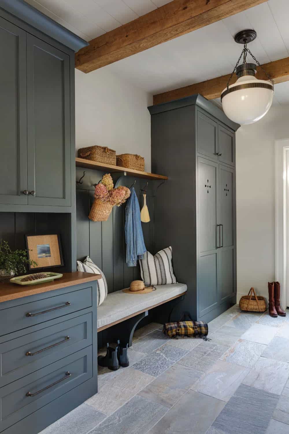 Mudroom with slate-blue cabinetry, a built-in bench with hooks, exposed beams, and stone floor tile