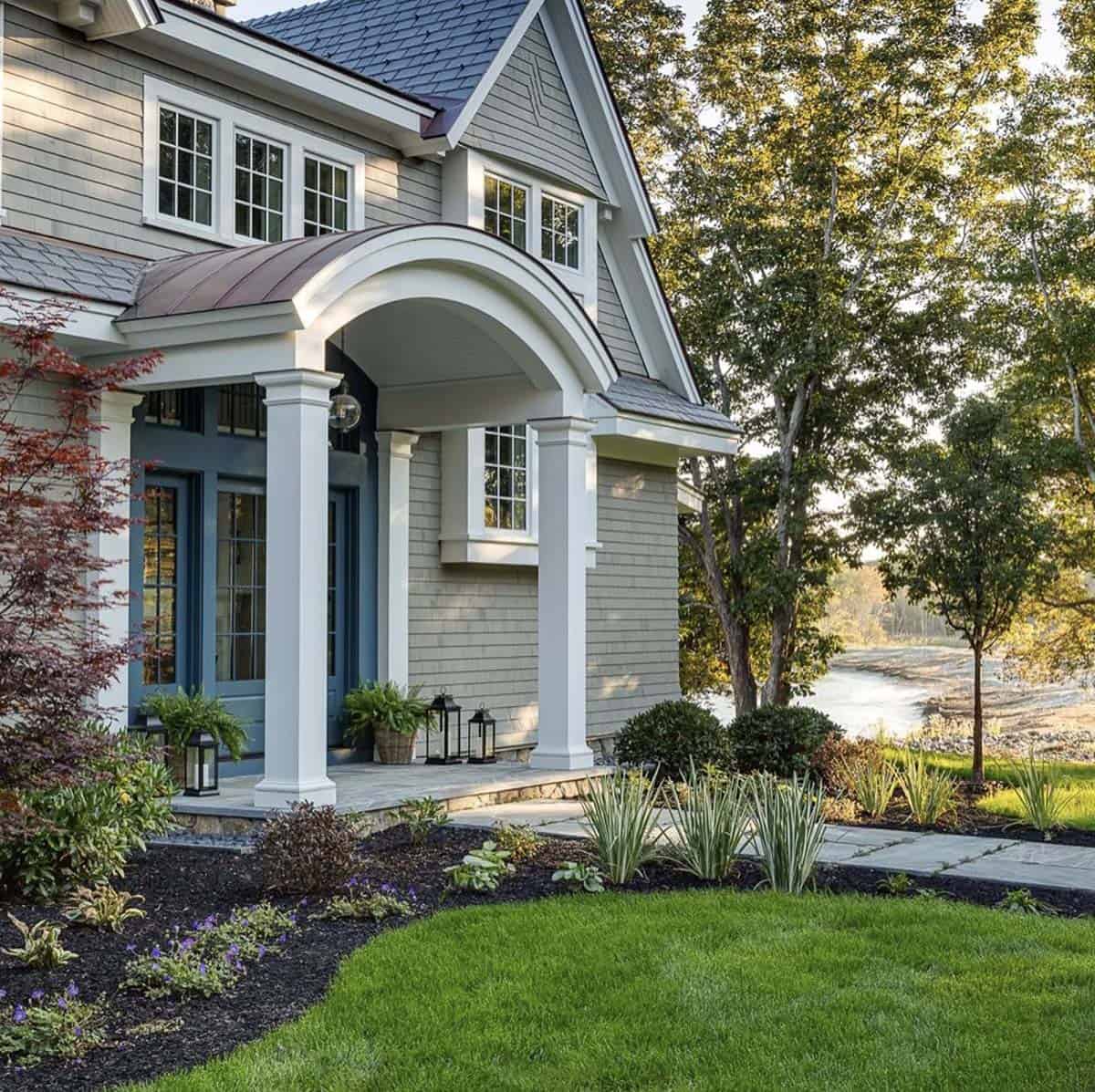 Arched copper-roofed portico with white square columns, blue double doors, and lanterns, with a tidal inlet beyond