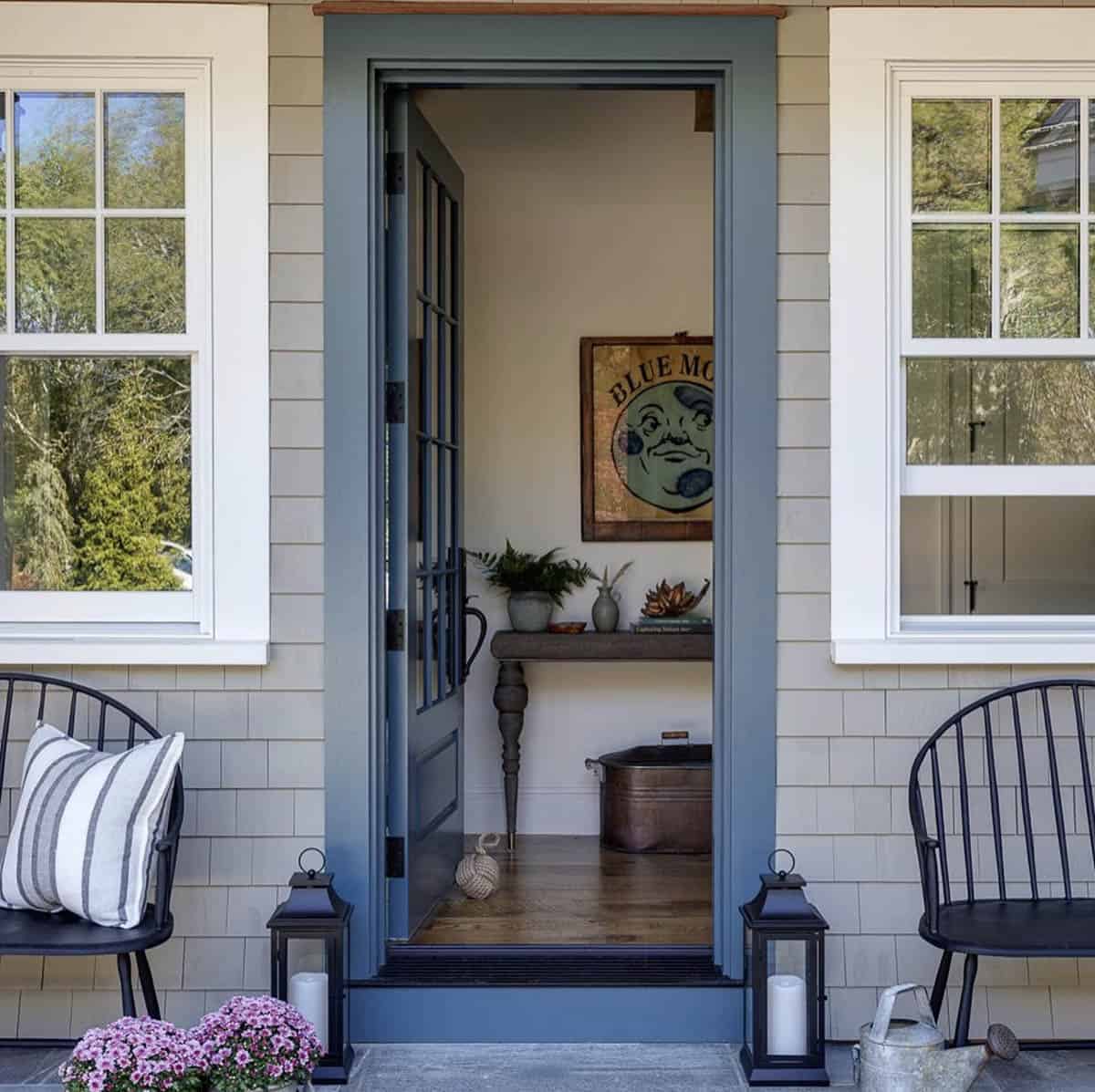 Open blue front door framed by shingled walls, with Windsor-style chairs, lanterns, and a "Blue Moon" sign visible inside