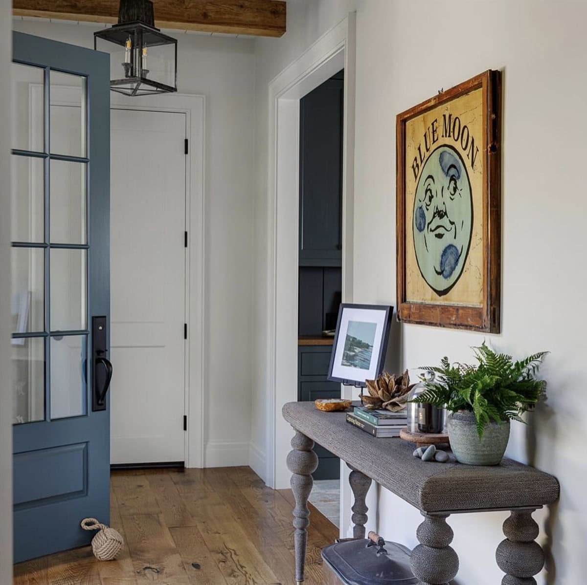 Entry hall with a glass-paned blue door, a rope-wrapped console table, and a vintage "Blue Moon" sign