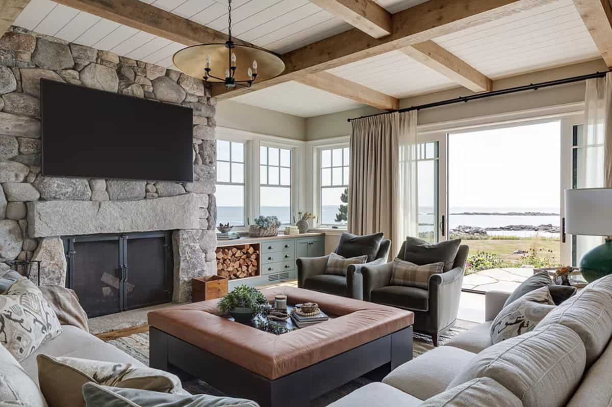Living room with a stone fireplace, timber-beamed ceiling, leather ottoman, and sliding doors to the ocean