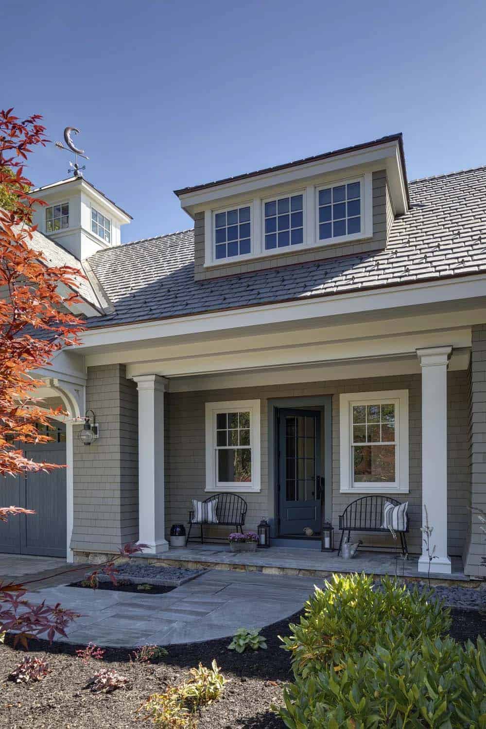 Garage-side entry porch with white columns, black Windsor benches, a blue door, and a cupola with a moon weathervane