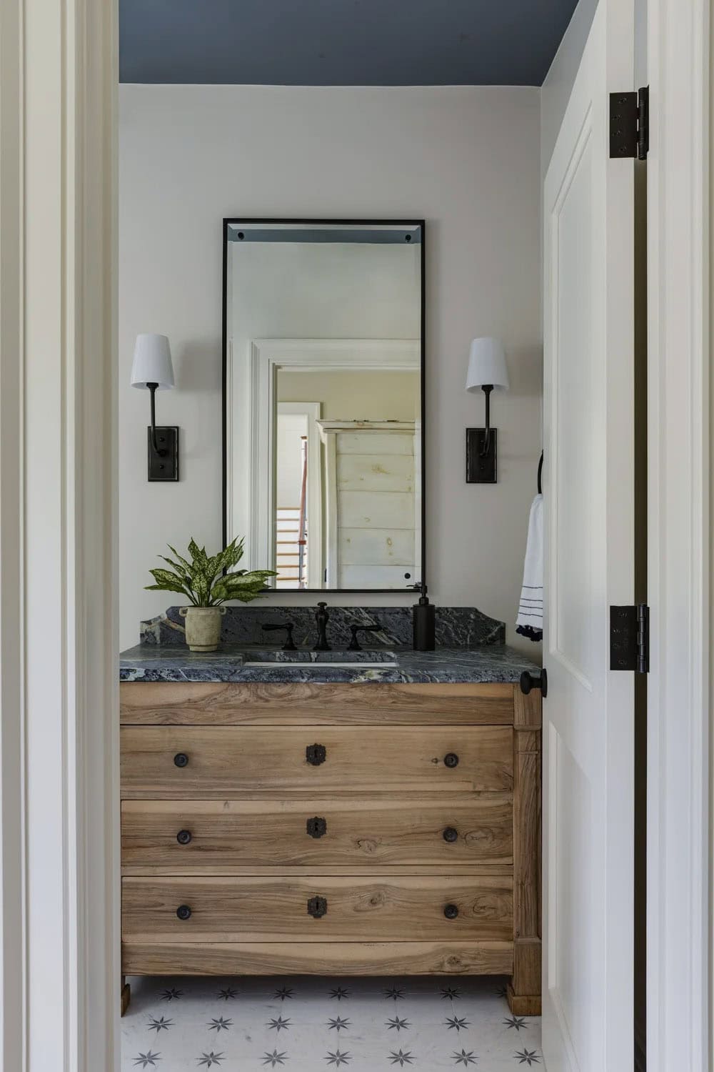 Powder room with a weathered wood vanity, a dark stone top, a black-framed mirror, and star-patterned floor tile