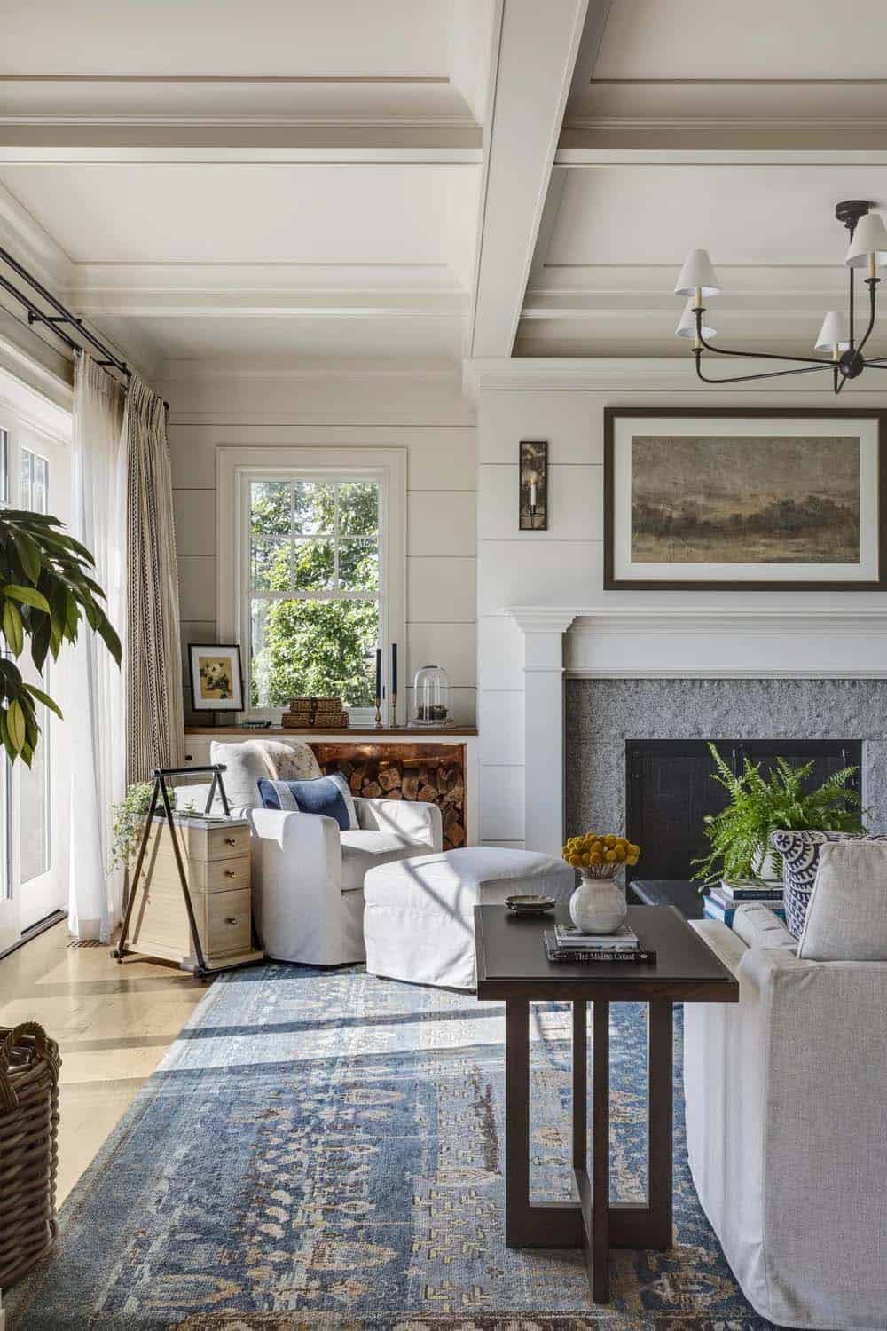 Living room with a coffered ceiling, shiplap walls, a granite fireplace, slipcovered seating, and a blue patterned rug