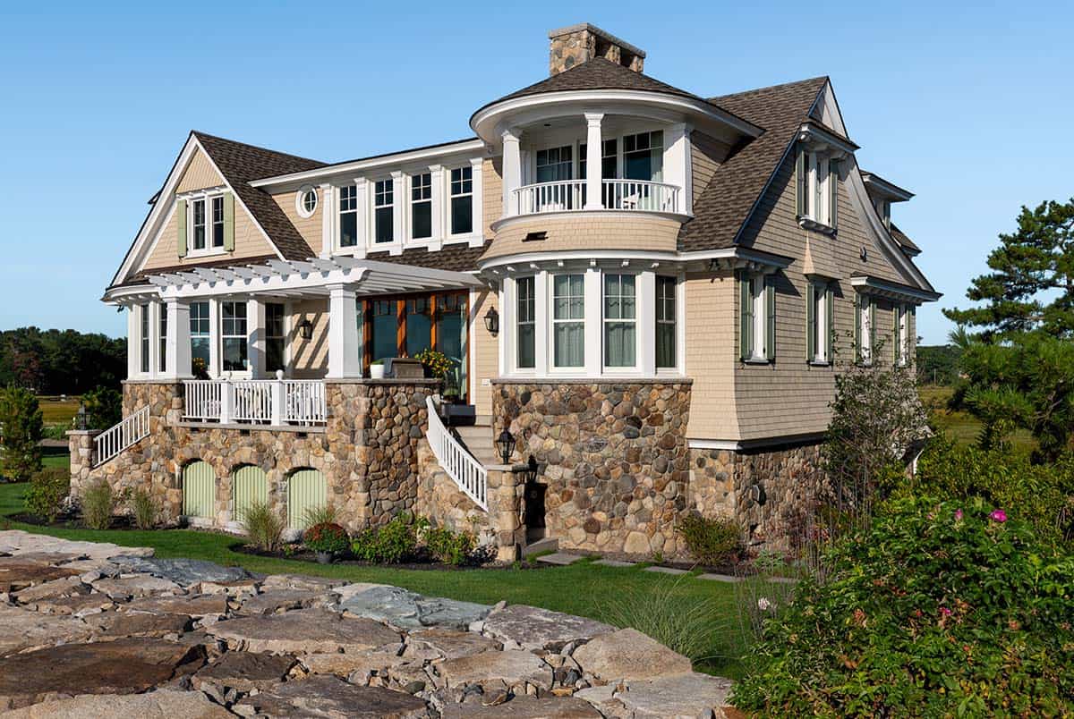 Side view of the shingled home with round balcony, stone foundation, and arched green doors