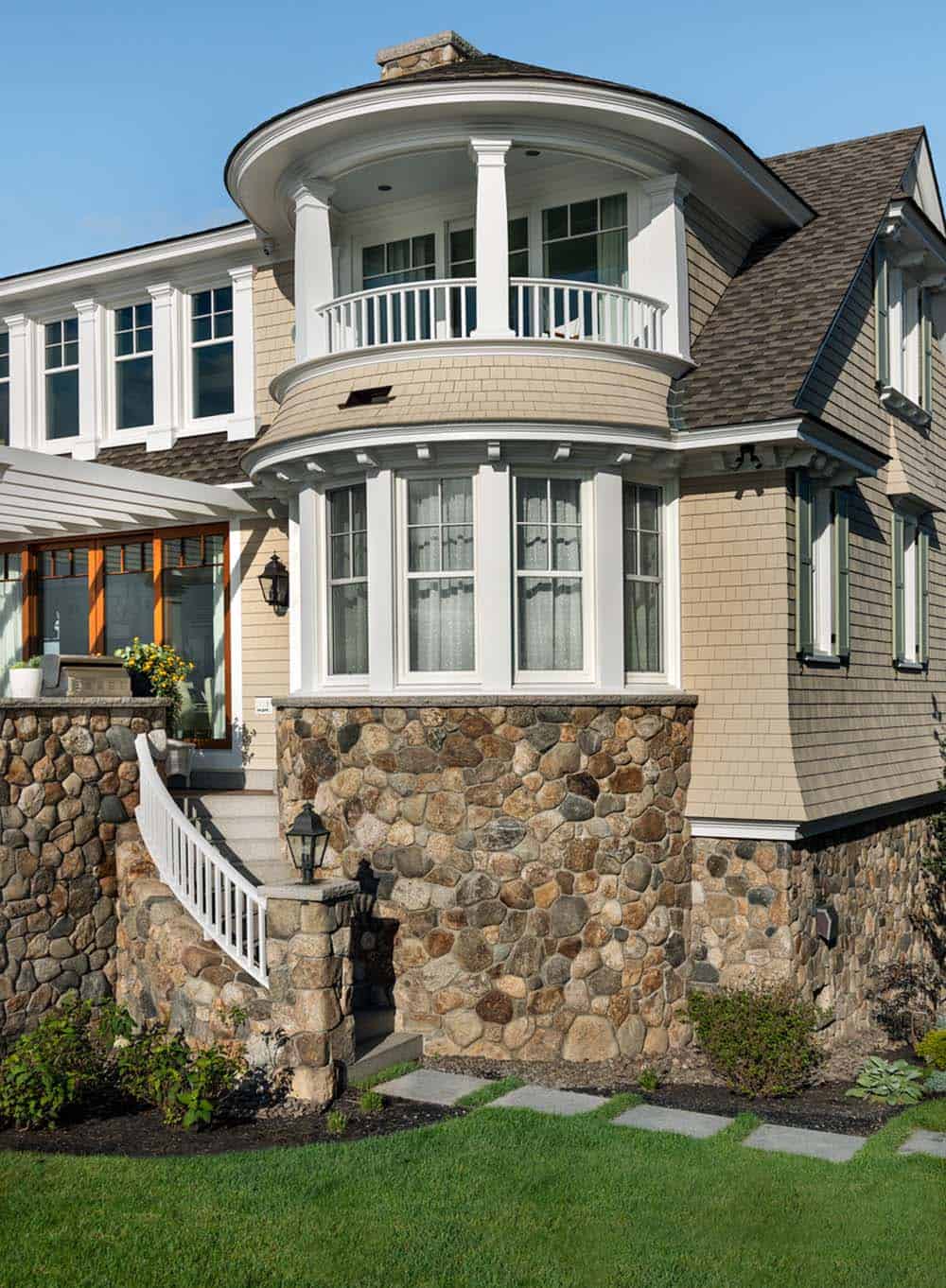Curved stone-base bay and rounded second-floor balcony with white railing
