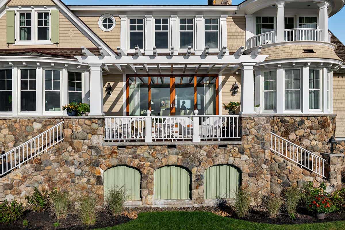 Covered porch with white pergola and wood-framed doors above a stone wall with three arched green doors
