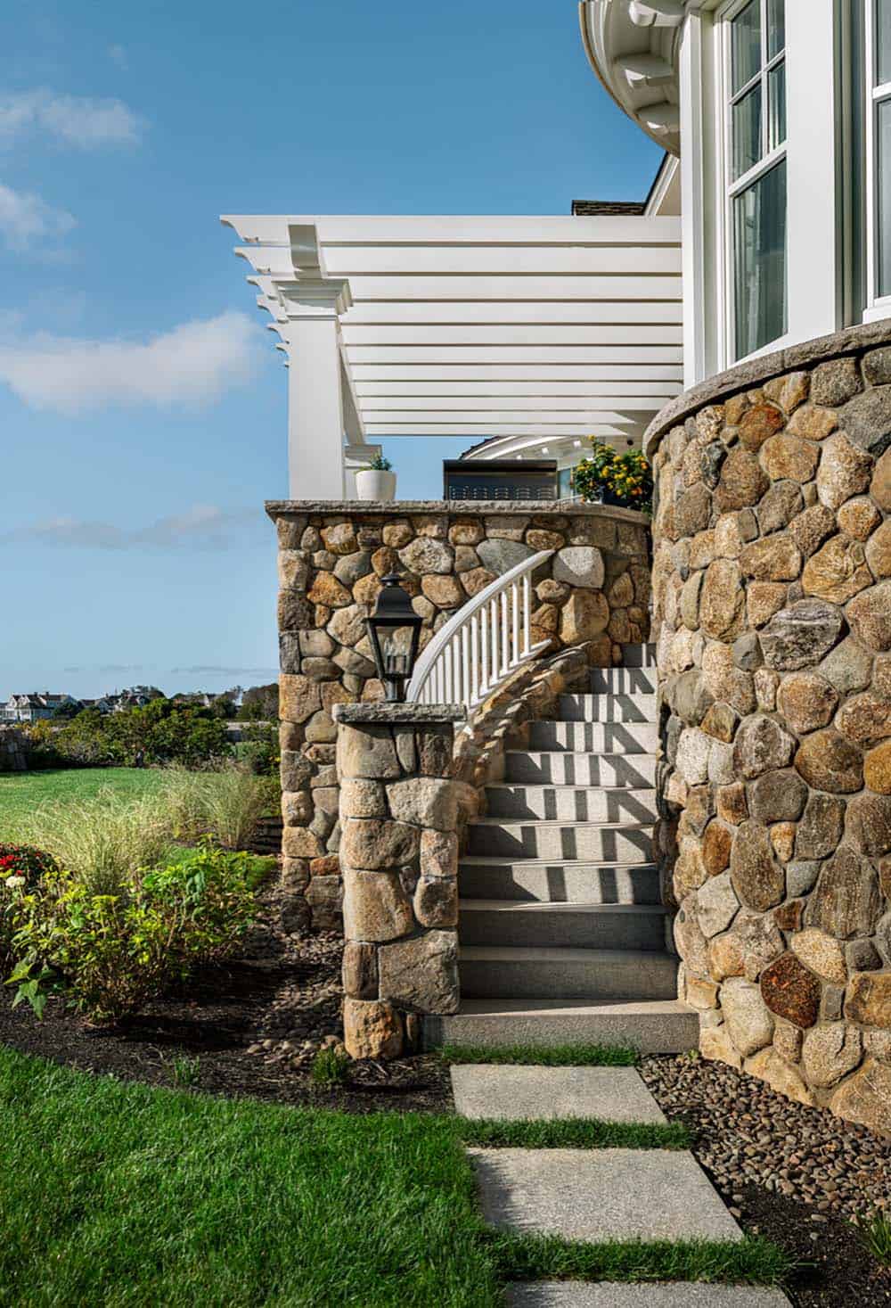 Curved granite staircase beside a stone wall and white pergola