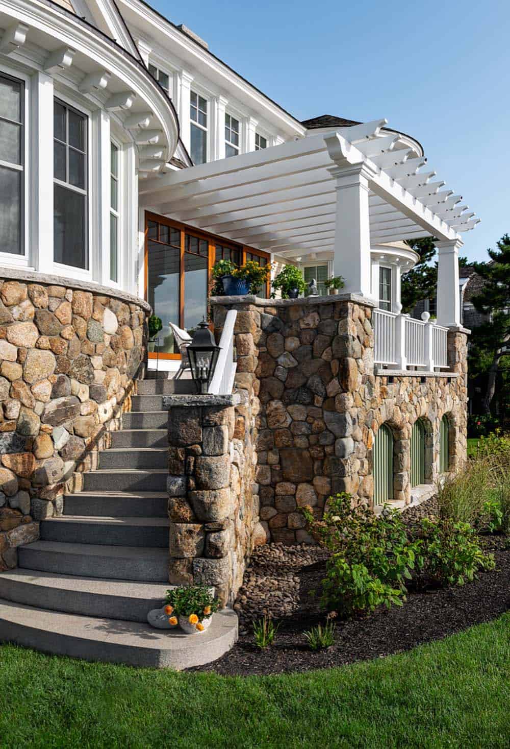 Stone entry steps with lantern and pergola-covered porch above arched green doors