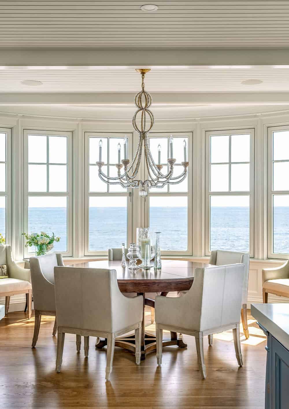 Round dining table and leather chairs under a beaded chandelier before ocean-facing windows