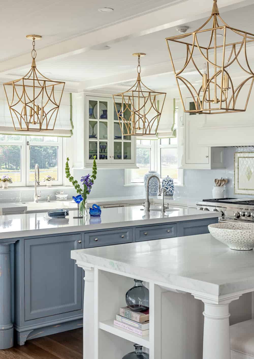 Kitchen island in dusty blue with gold lantern pendants and glass-front cabinets