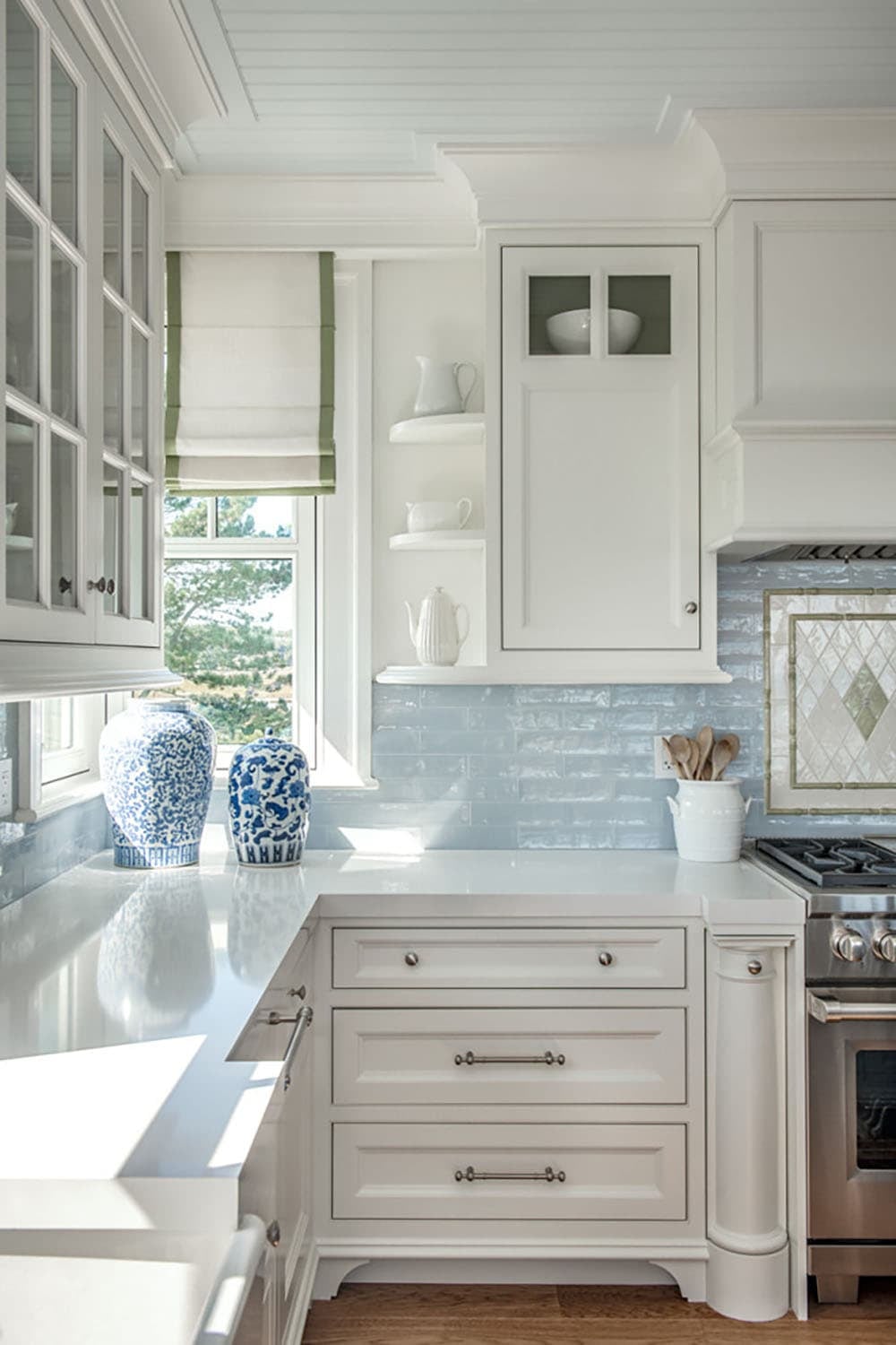 Kitchen corner with blue-and-white ginger jars, open corner shelves, and green-trimmed Roman shade