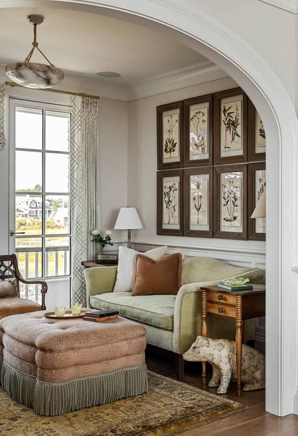 Sitting nook with green velvet sofa, pink tufted ottoman, and framed pressed botanicals