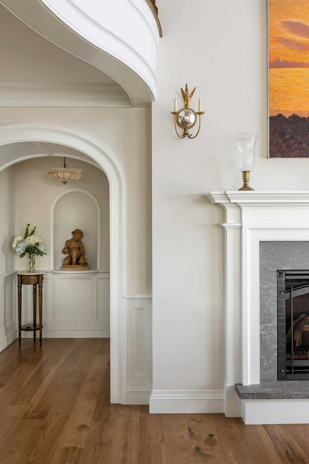 Arched alcove with a statue and side table beside the fireplace and sunset painting
