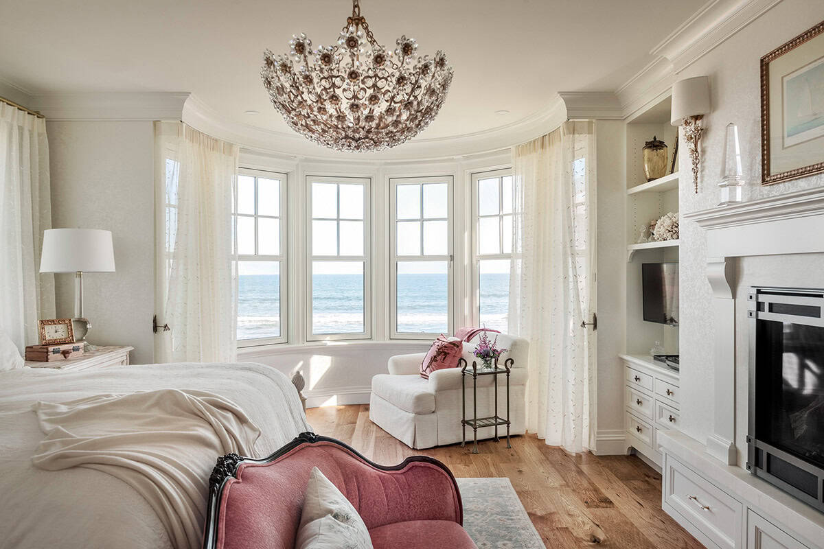 Primary bedroom with a crystal flower chandelier and curved window bay facing the ocean