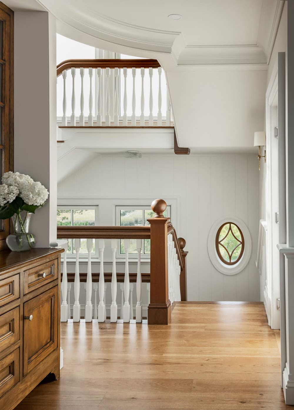 Staircase landing with wood handrail, white balusters, and oval window