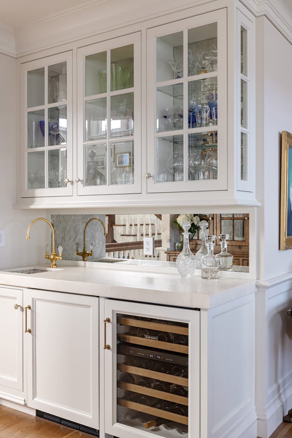 Wet bar with glass-front cabinets, mirrored backsplash, brass faucets, and wine fridge