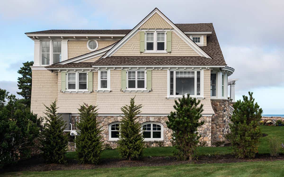 Side view of the shingled home with green shutters and a stone base with arched windows