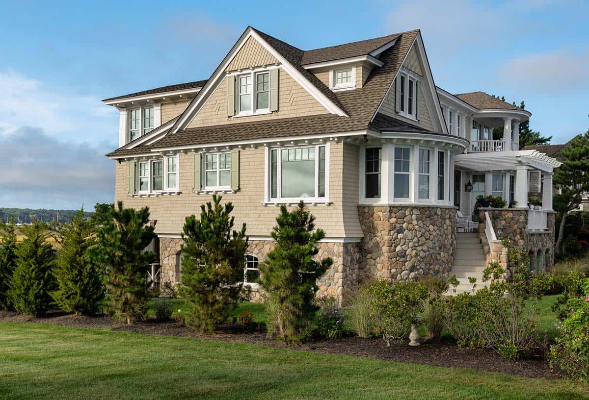 Corner view of the shingled house with a rounded stone bay and pine trees in the foreground