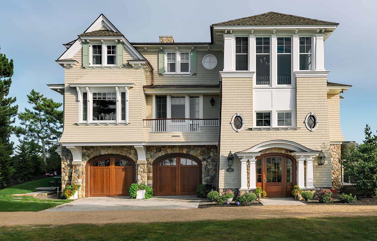 Front of the home with arched wood garage doors, round windows, and a stone base