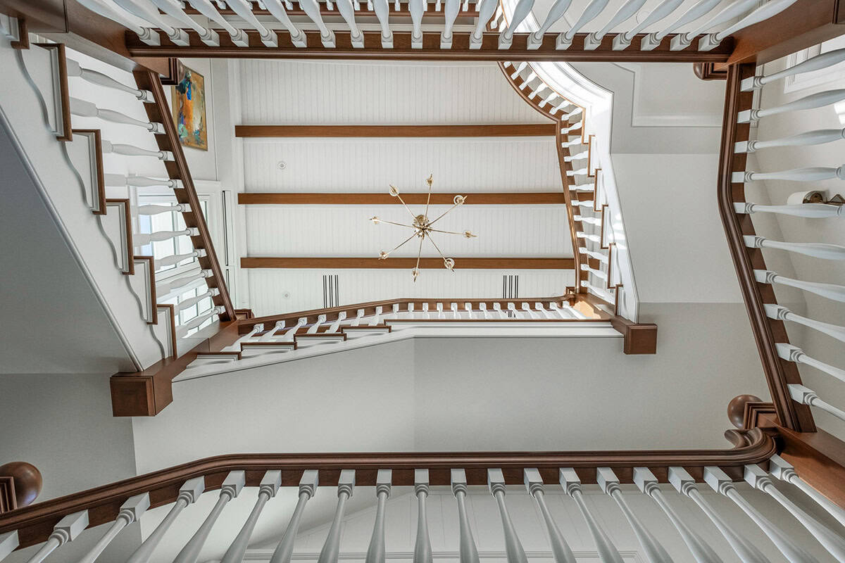 Looking up a stairwell with wood handrails, white balusters, and exposed beams