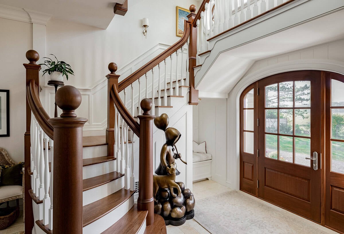 Entry foyer with curved staircase, arched wood door, and bronze sculpture
