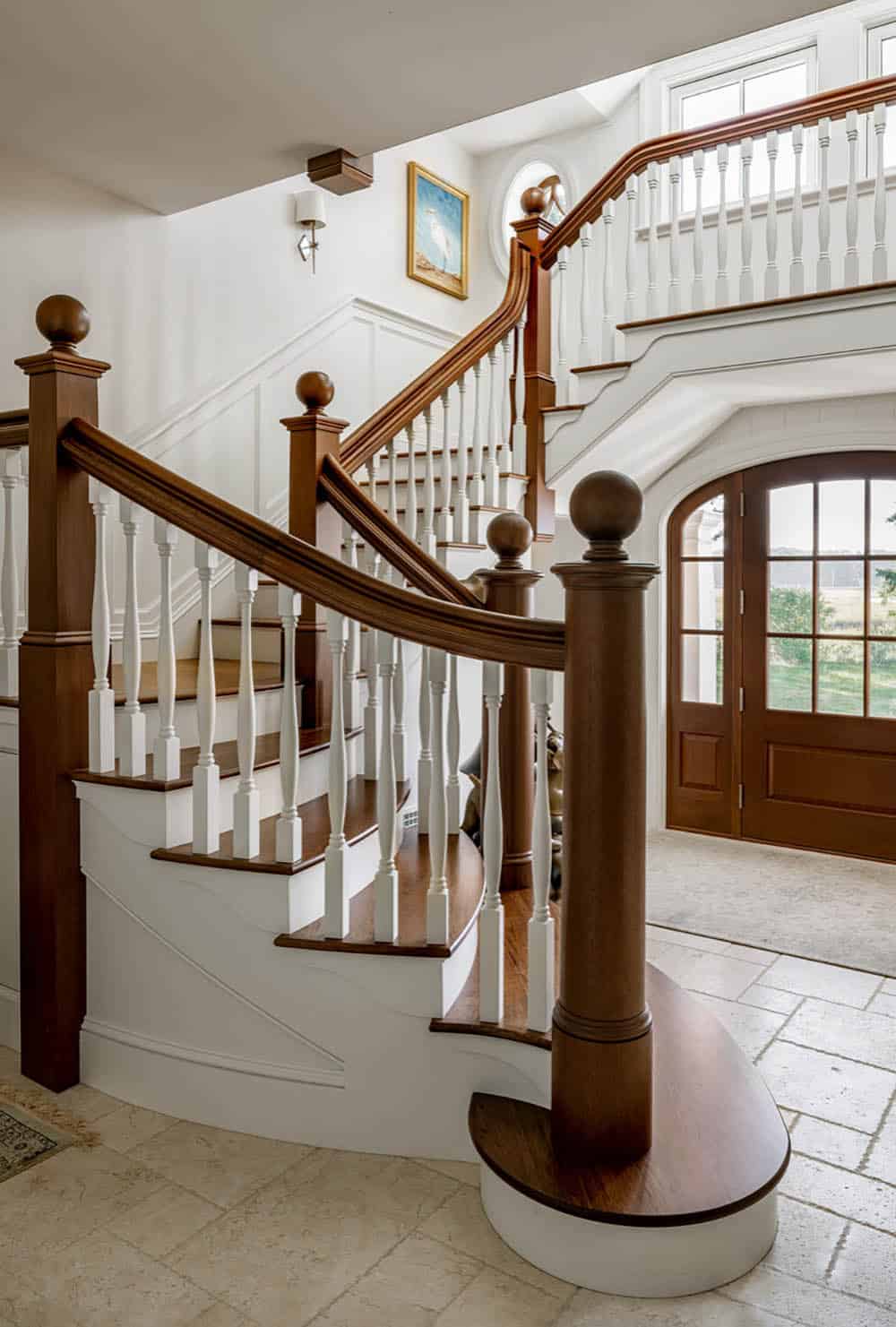 Curved staircase with wood newel posts and white balusters beside the arched front door