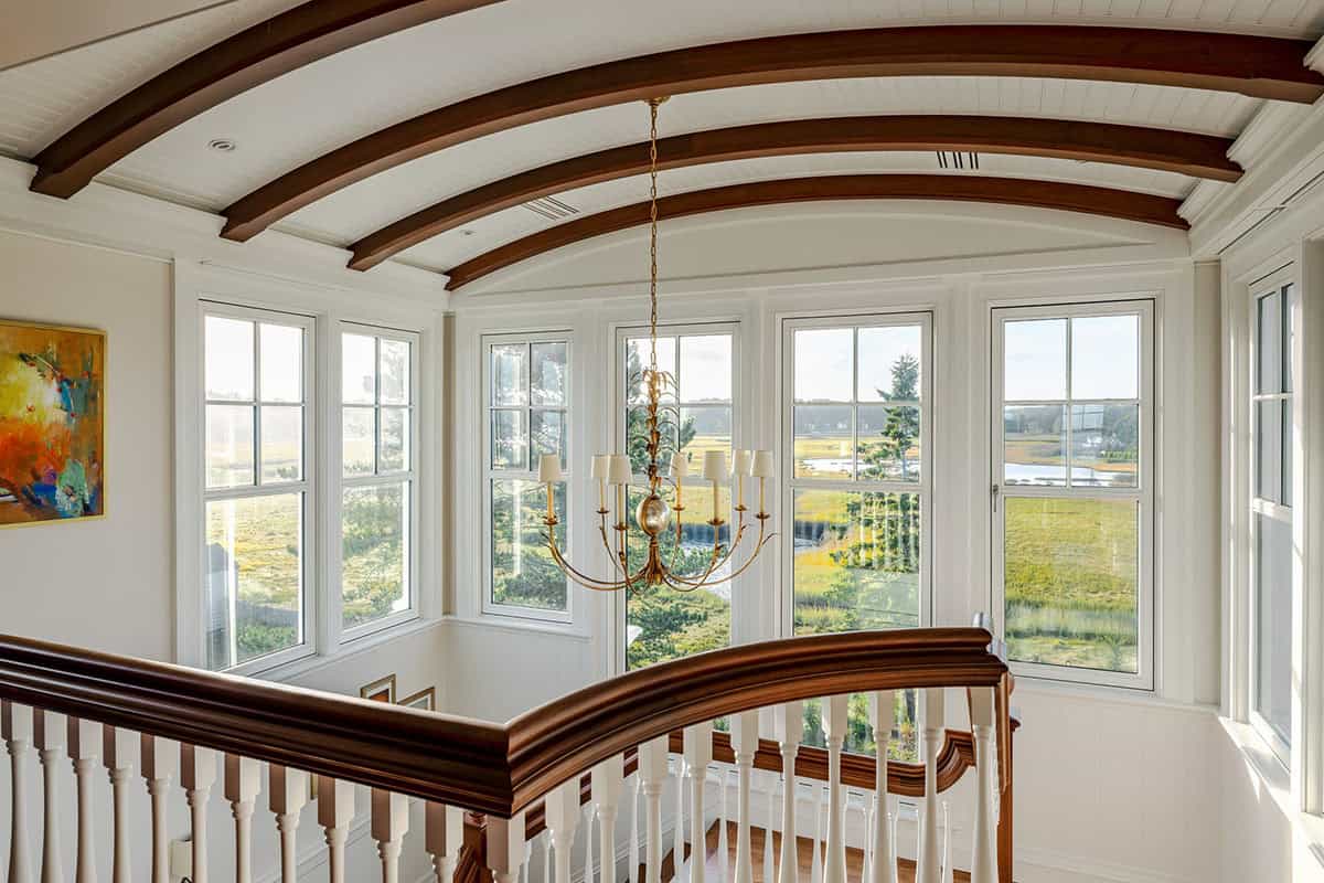 Stair landing under a barrel-vaulted ceiling with curved wood beams and a gold chandelier