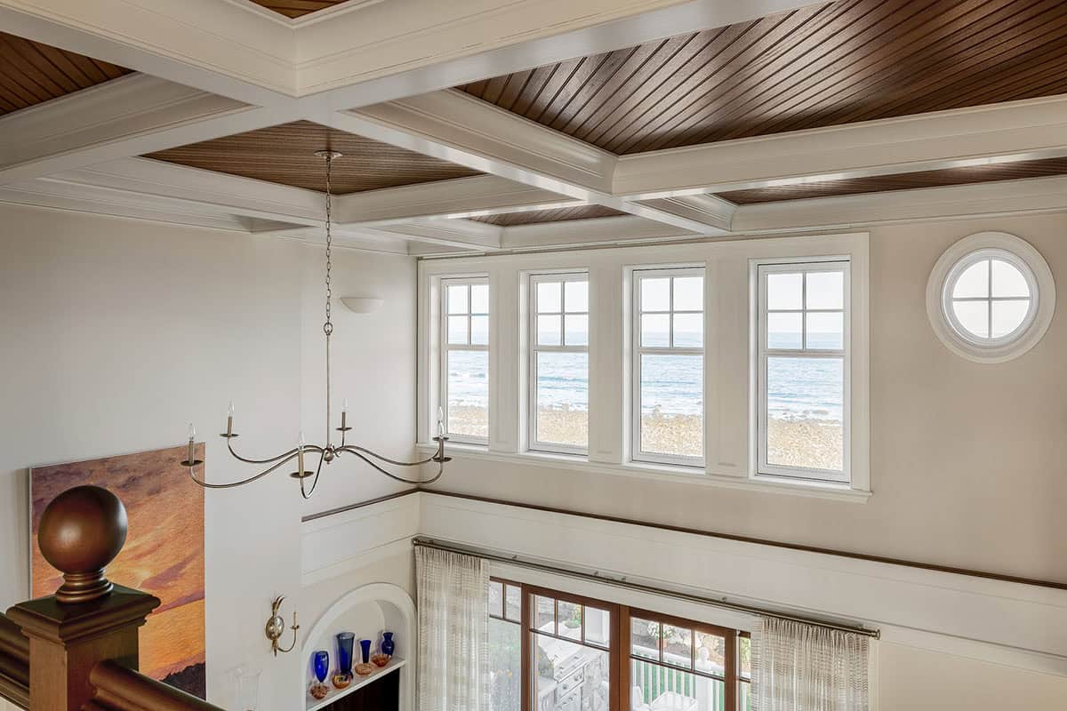 View down to the living room from above, with coffered ceiling and ocean-facing windows