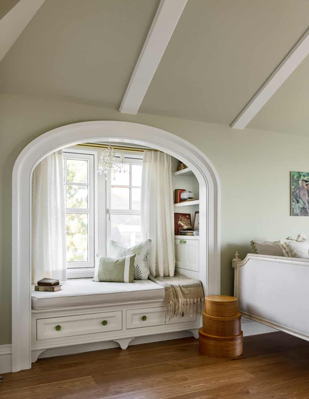 Arched window seat with built-in shelves and drawers in a sage green bedroom