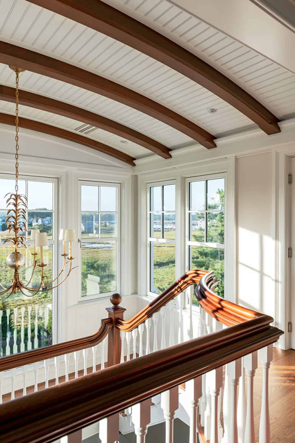 Stair landing with curved wood handrail, barrel-vaulted beamed ceiling, and gold chandelier