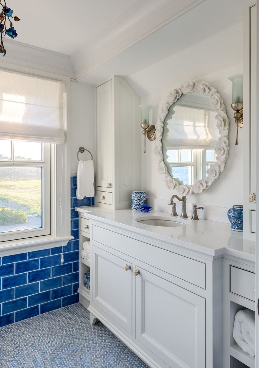 Bathroom with deep blue tile wainscot, white vanity, and floral mirror