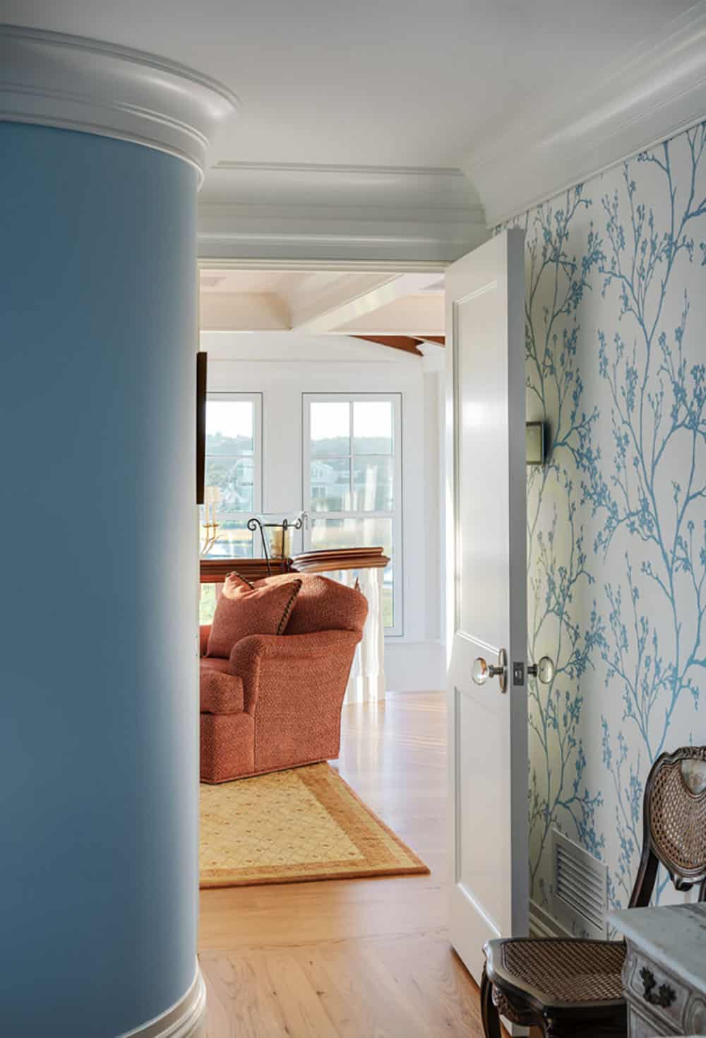 Hallway with powder blue curved wall and branch-patterned wallpaper, opening to a sitting room