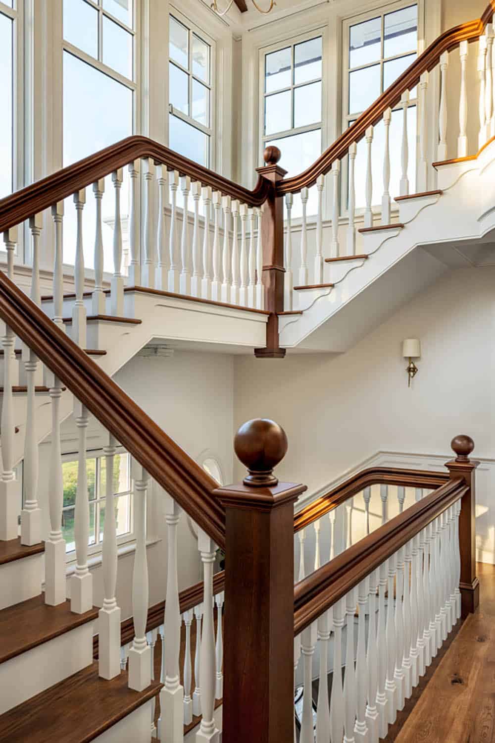 Open staircase with dark wood handrail, white balusters, and tall windows