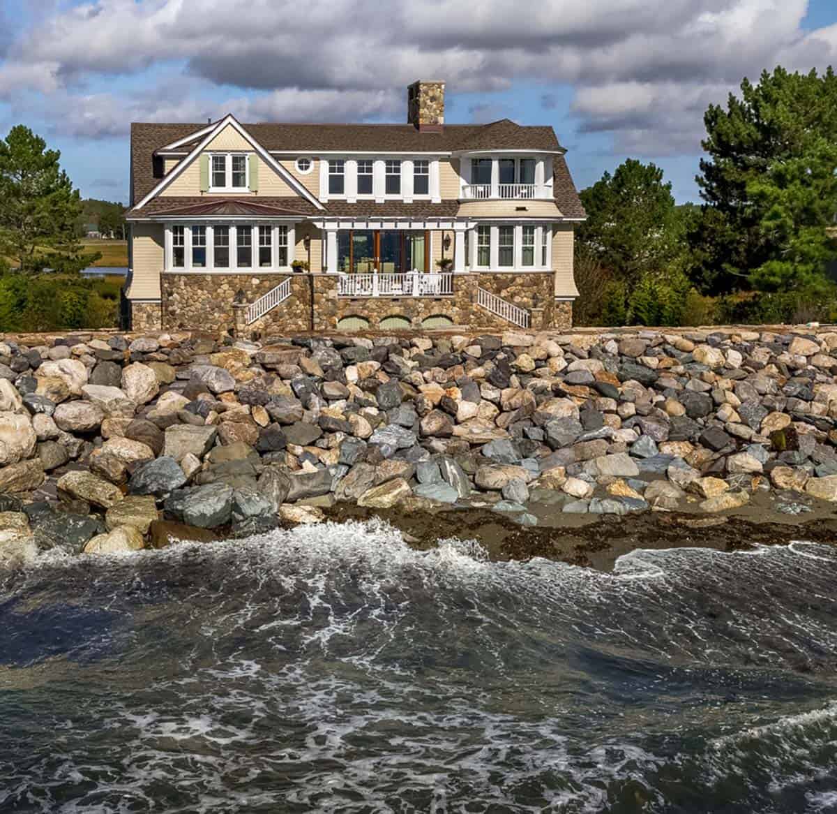 Front-facing view of the house, stone base, and pergola behind a rocky seawall