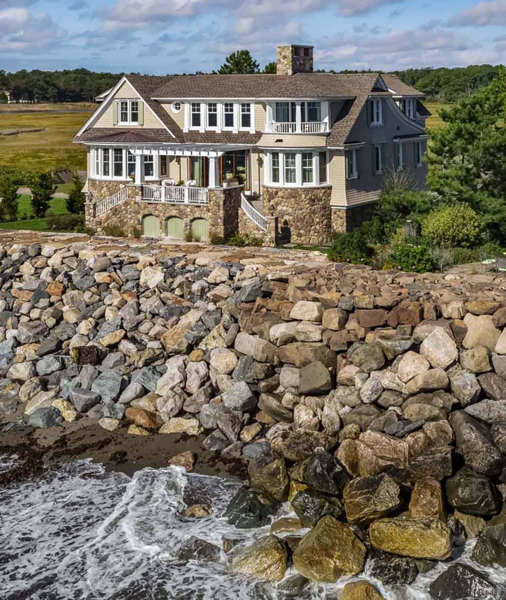Angled view of the house above the boulder seawall, with a rounded stone bay and white porch