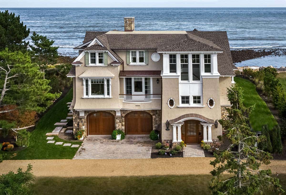 Aerial view of the home's entry side, with arched garage doors, gravel drive, and ocean beyond