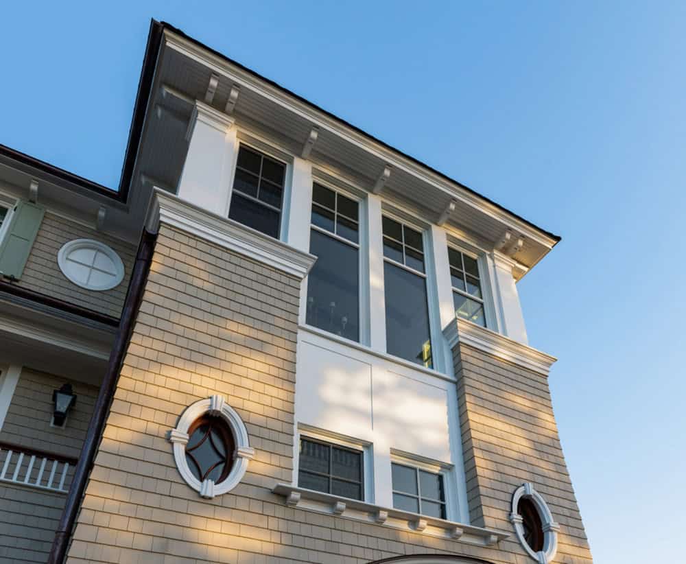 Upward view of shingled tower with tall windows, oval windows, and white trim