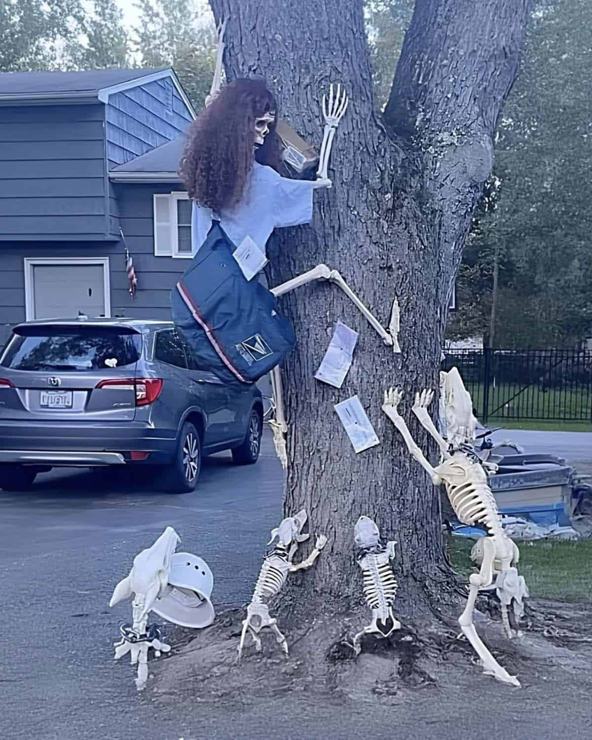 Skeleton mail carrier with long curly hair and a mailbag climbing a tree while skeleton dogs claw at the trunk below