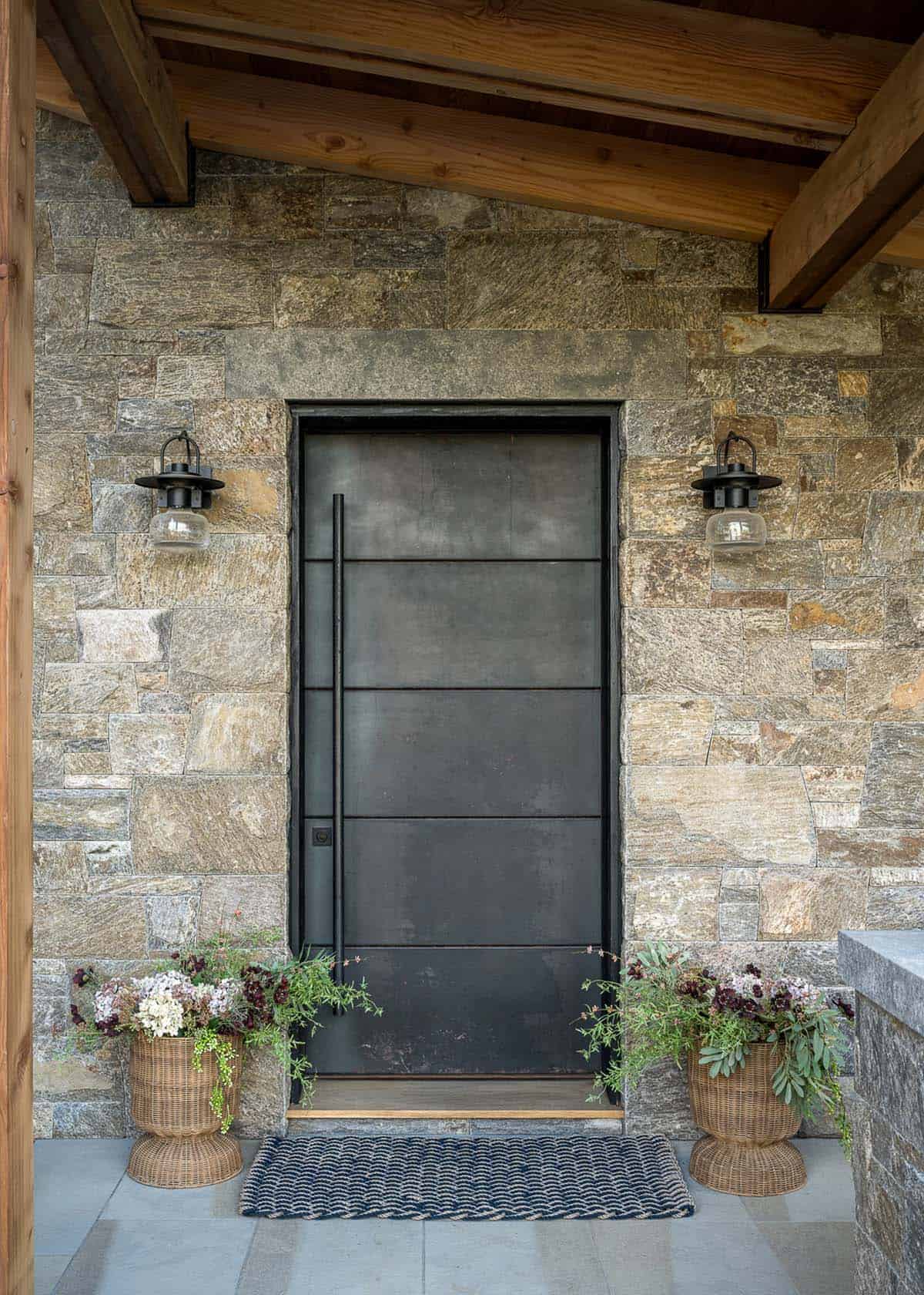 Custom blackened steel front door set in stone wall with lantern sconces