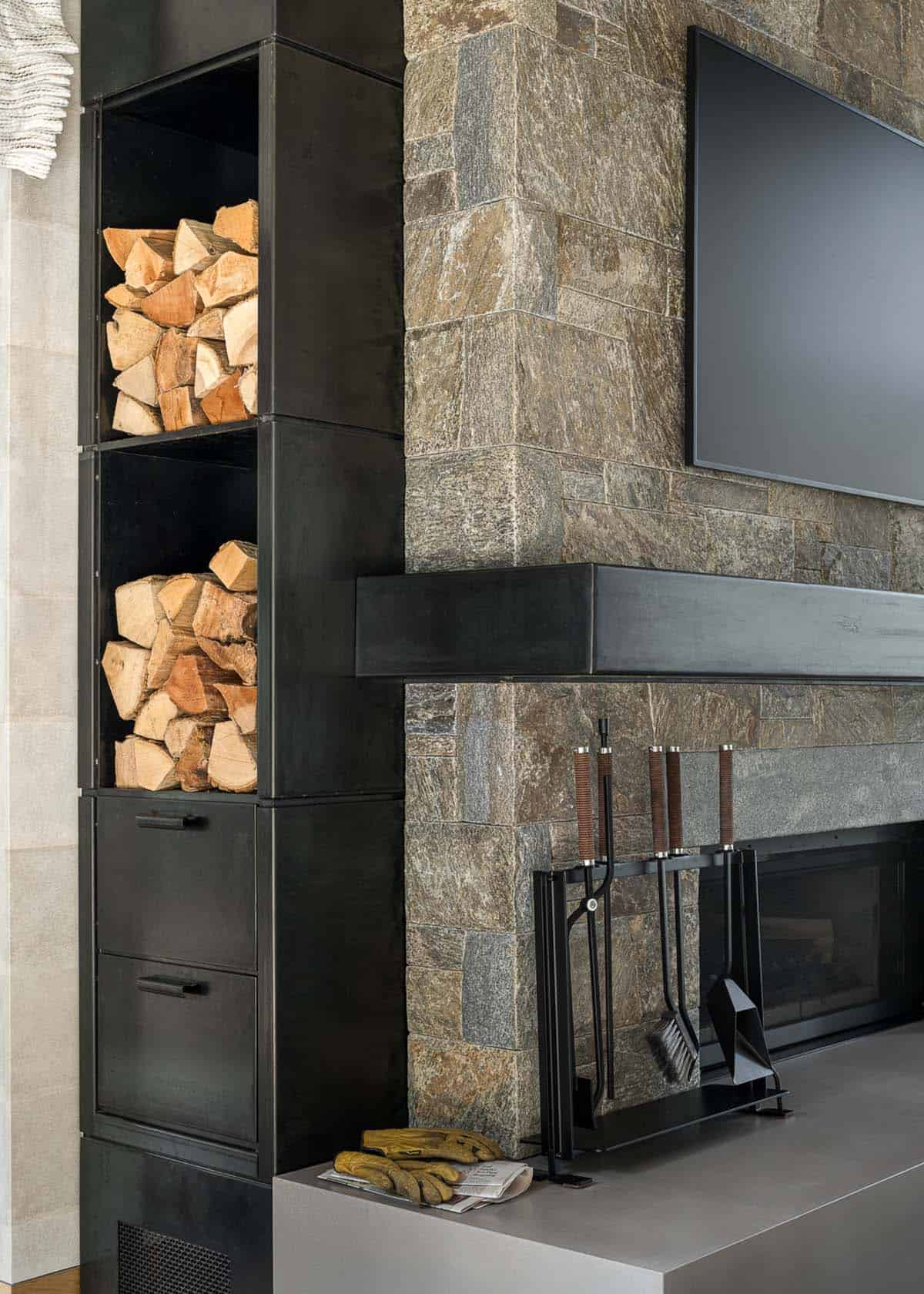 Blackened steel firewood storage beside stone fireplace and steel mantel